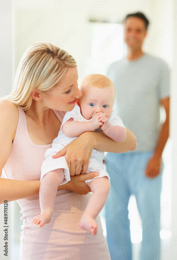 Mommys here, my girl. A doting mother holding her cute little girl while her husband stands in the b