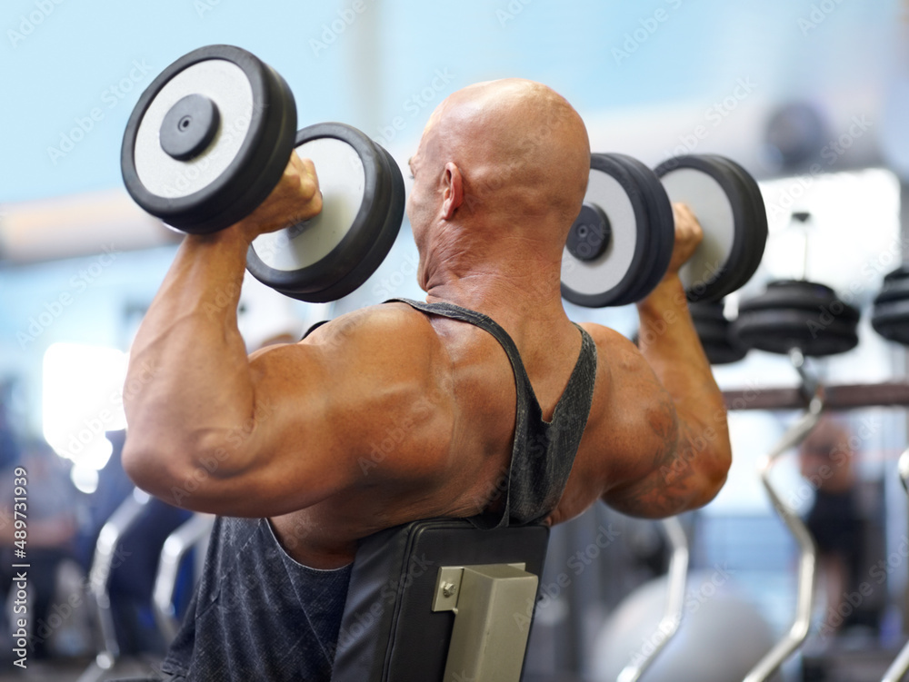 Pushing himself hard. Shot of a male bodybuilder lifting weights at the gym.