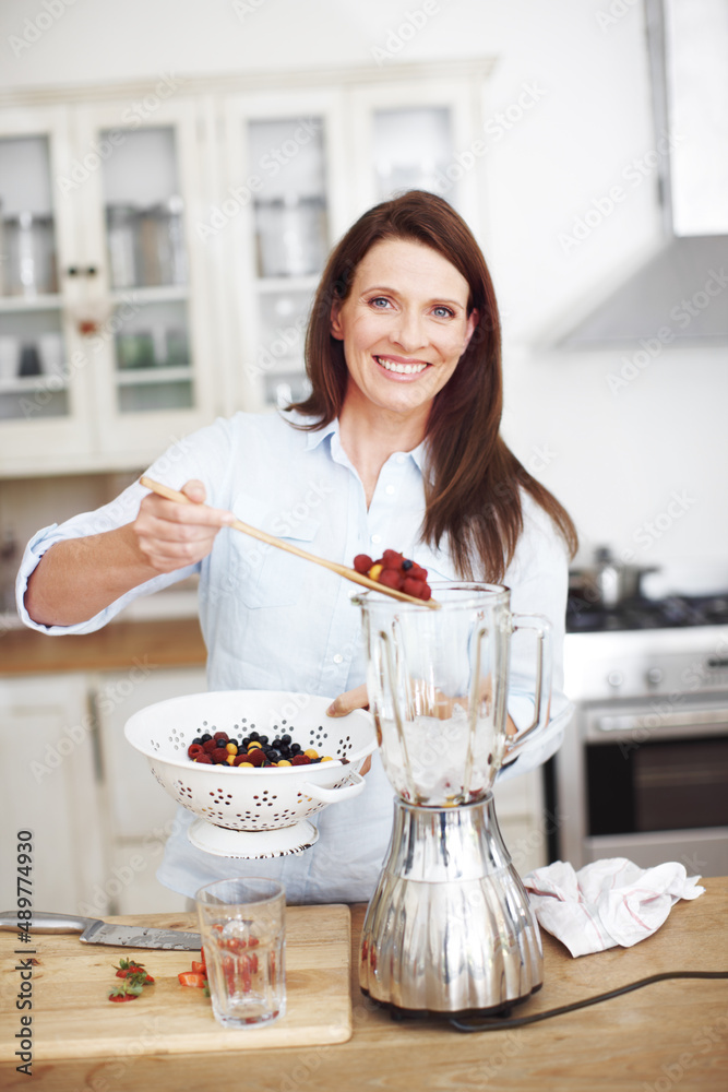 Fruit Scoop. An attractive woman adding fruit to a blender while standing at a kitchen counter.