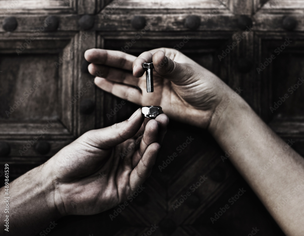 A helping hand. Closeup of two hands holding a nut and bolt against a wooden door.