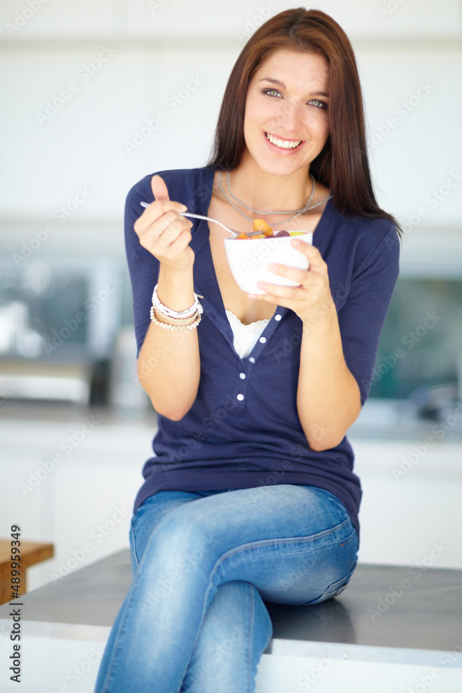 Indulging in a healthy snack. Portrait of a smiling young woman eating a healthy fruit salad for lun