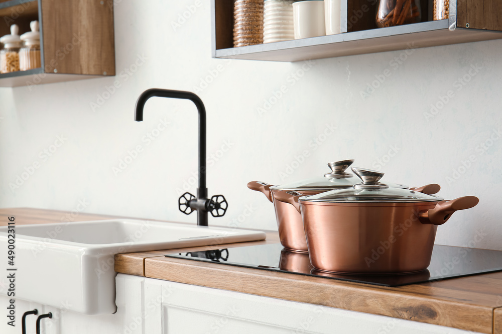 Shiny cooking pots on stove near light wall in kitchen