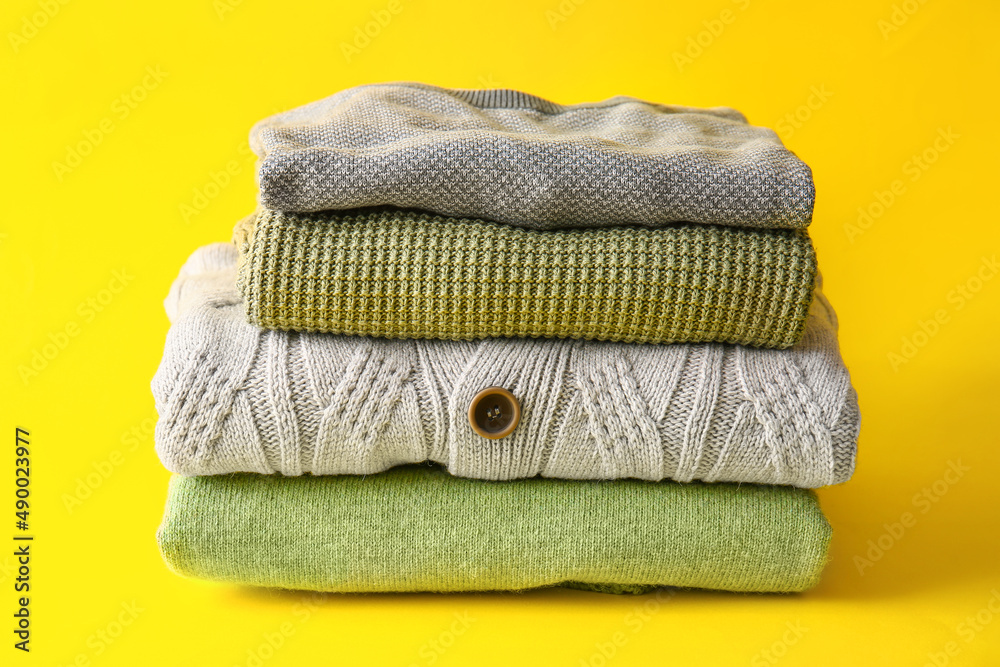 Stack of stylish sweaters on yellow background