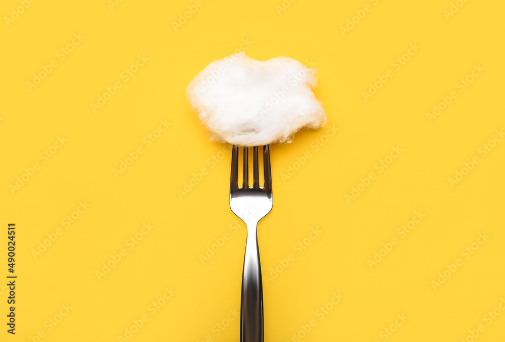 Fork with cotton wool on yellow background