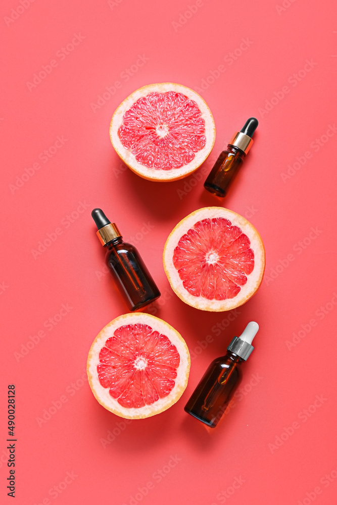 Composition with bottles of essential oil and ripe grapefruits on color background