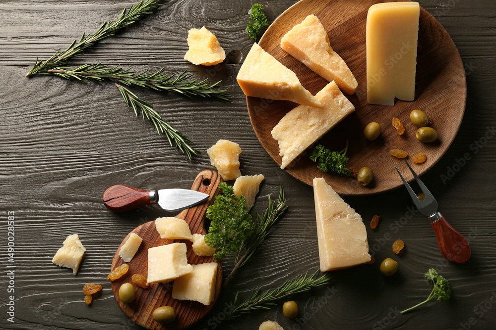 Plate and board with pieces of tasty Parmesan cheese on brown wooden background