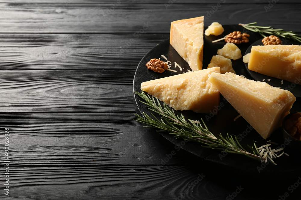 Board with pieces of tasty Parmesan cheese on black wooden background, closeup