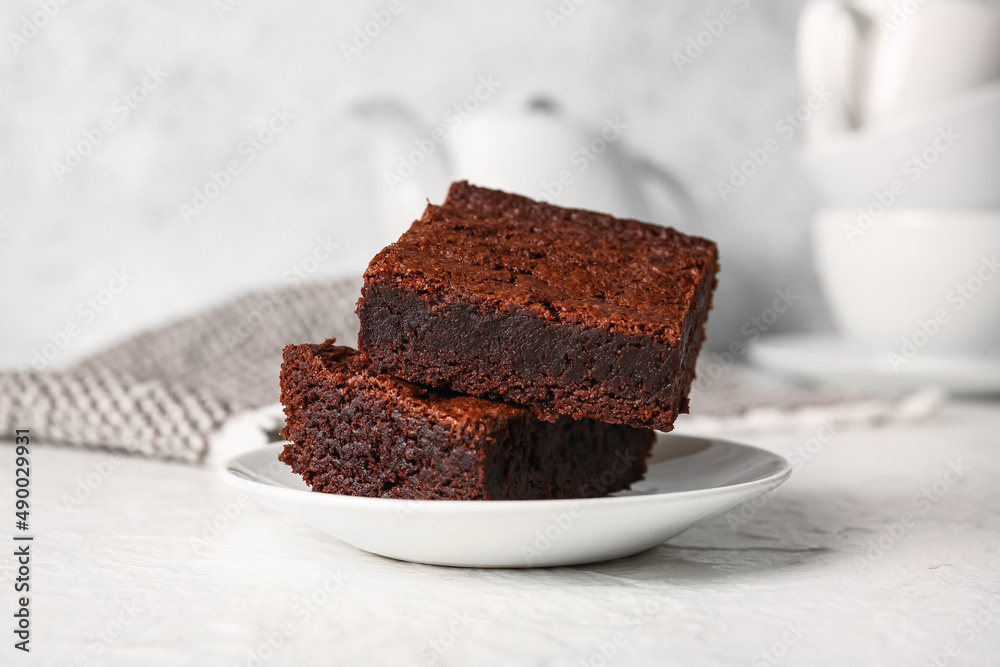 Plate with pieces of delicious chocolate brownie on light background