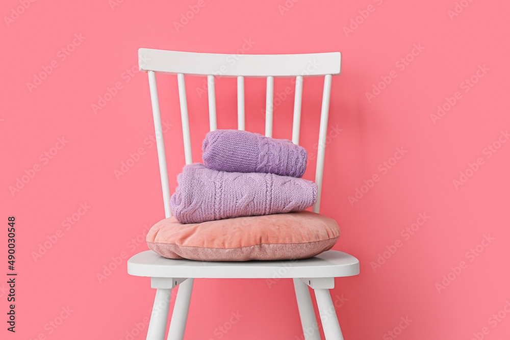 Stack of folded lilac sweaters on chair near color wall