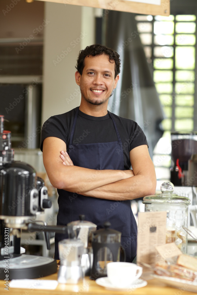 Hes a master fo brewing. Shot of a handsome barista standing behind his coffee bar with his arms cro