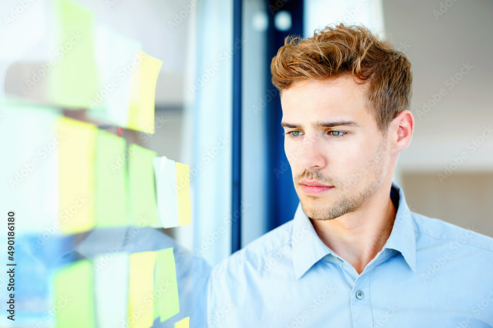 Thoughtful guy looking at adhesive notes. Thoughtful business man looking at adhesive notes on glass