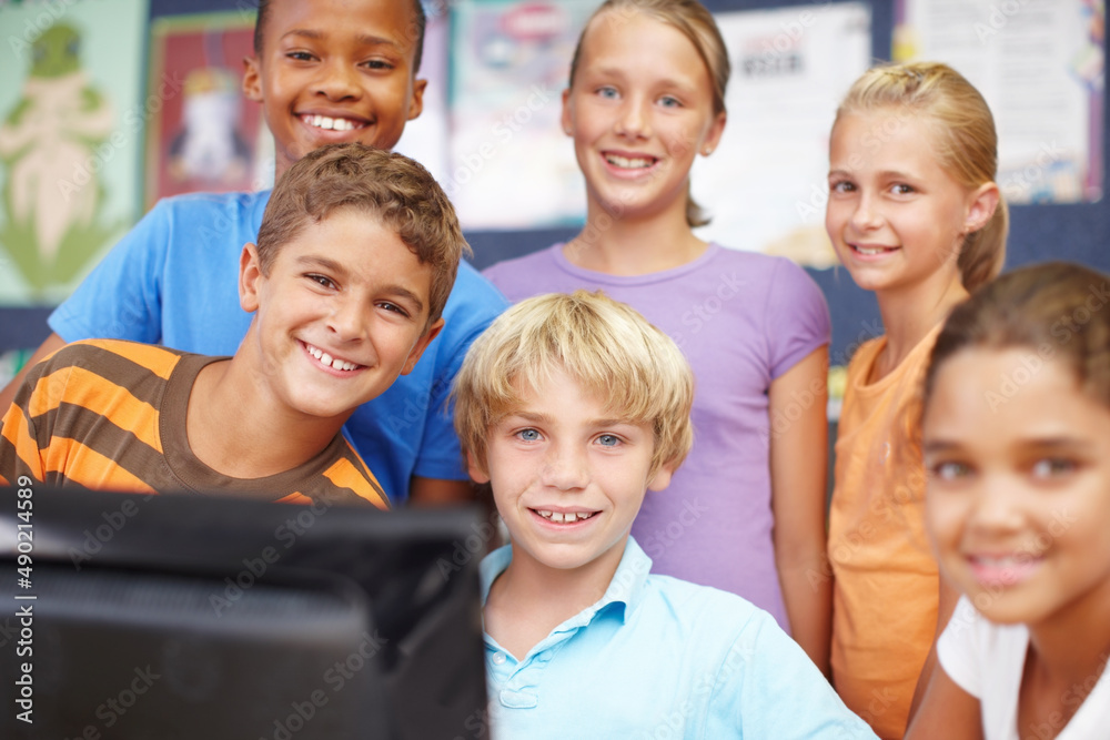 We love computer class. Portrait of a group of cute kids sitting and standing around a computer duri