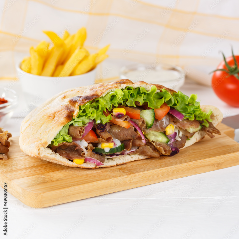 Döner Kebab Doner Kebap slice fast food in flatbread with French Fries on a wooden board square