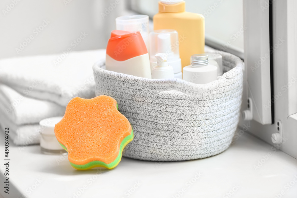 Bath sponge and basket with different cosmetic products on windowsill