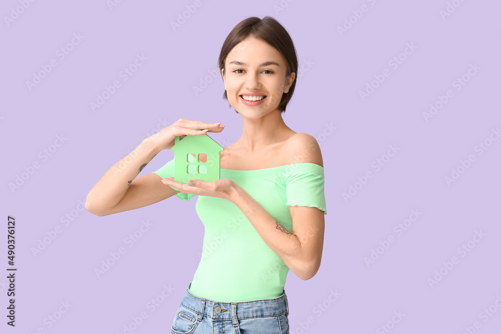 Beautiful young woman with figure of house on color background