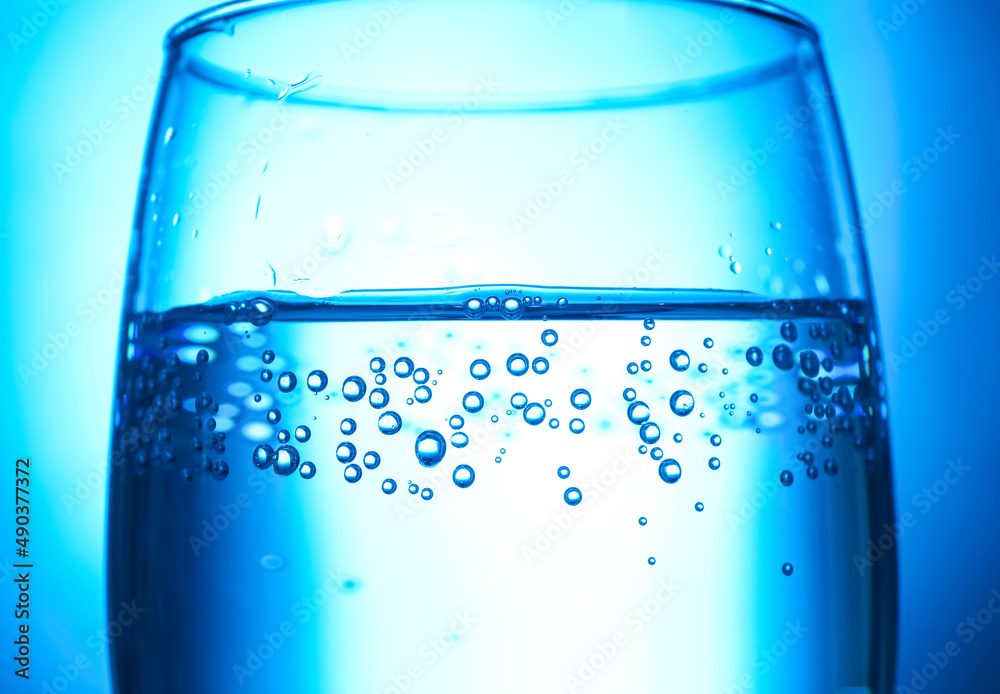 Glass of clear water on blue background, closeup