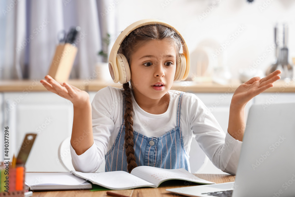 Confused little girl in headphones studying with online tutor at home