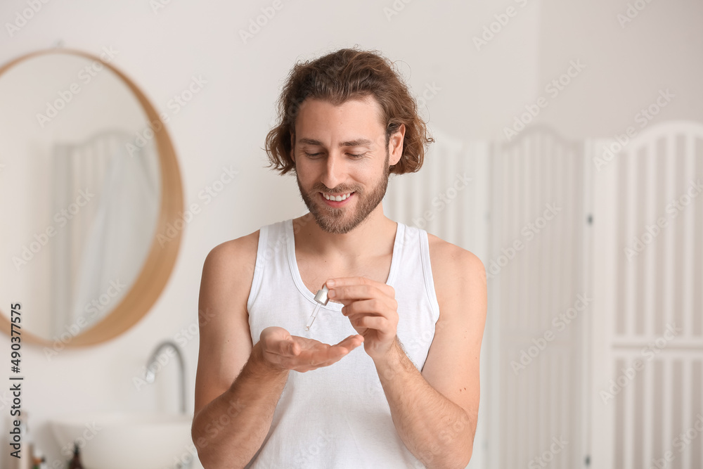 Young man using serum for skin care in bathroom