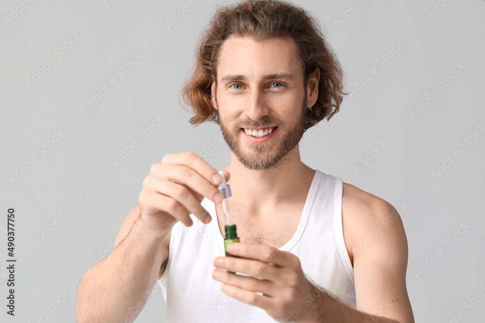 Young man with serum for skin care on grey background