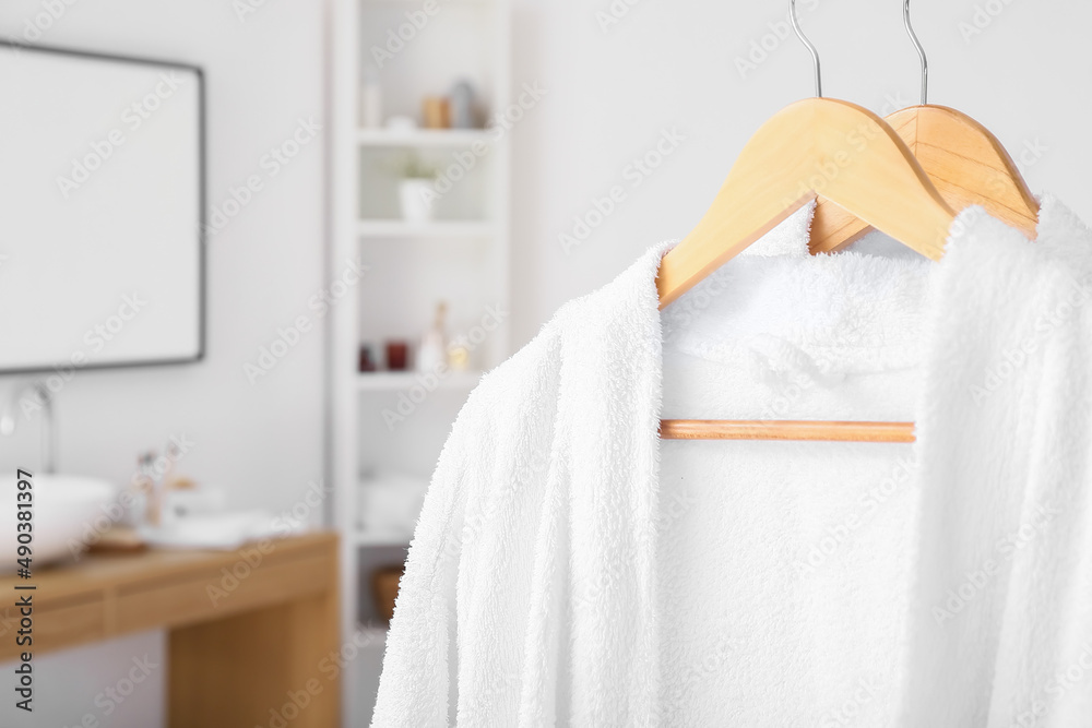 Hangers with soft bathrobes in light bathroom, closeup