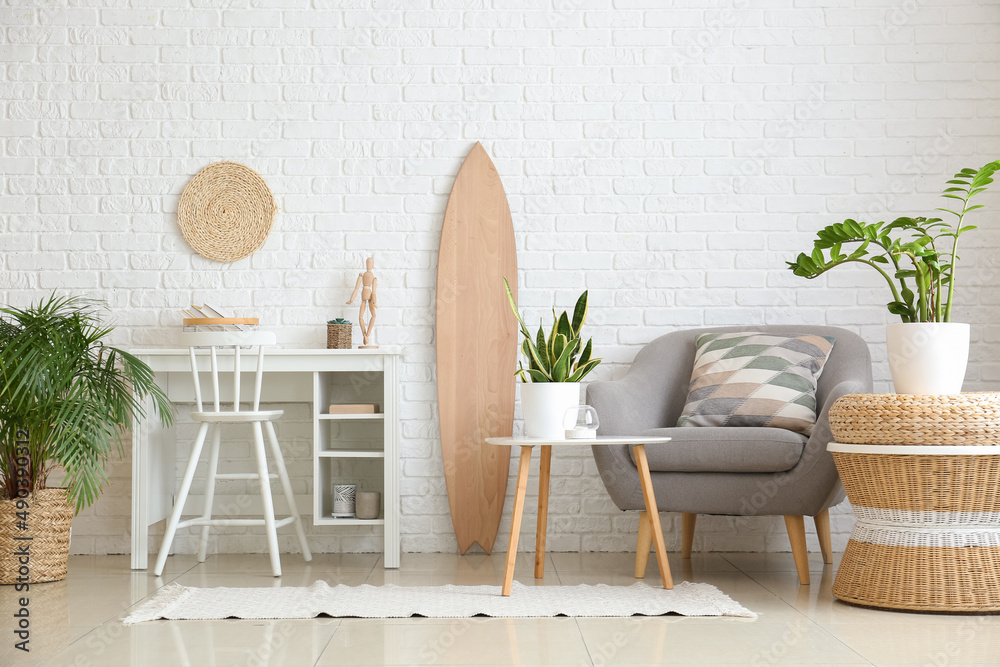 Interior of light living room with wooden surfboard, workplace and houseplants