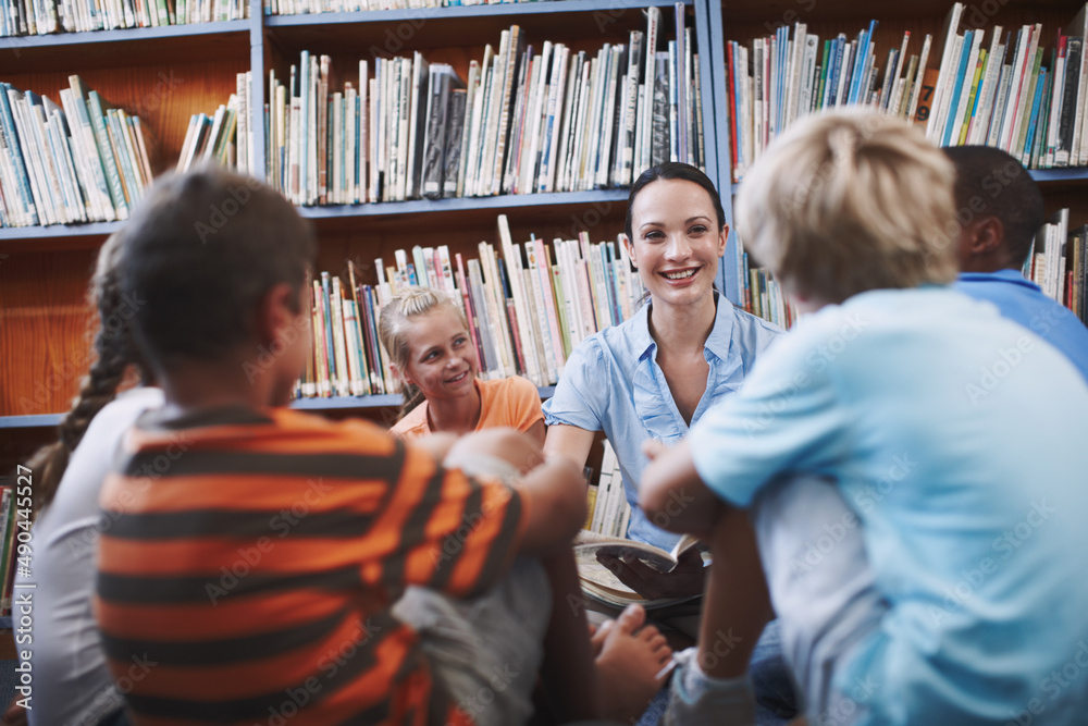 Learning together. A pretty teacher sitting with her excited students in the library.