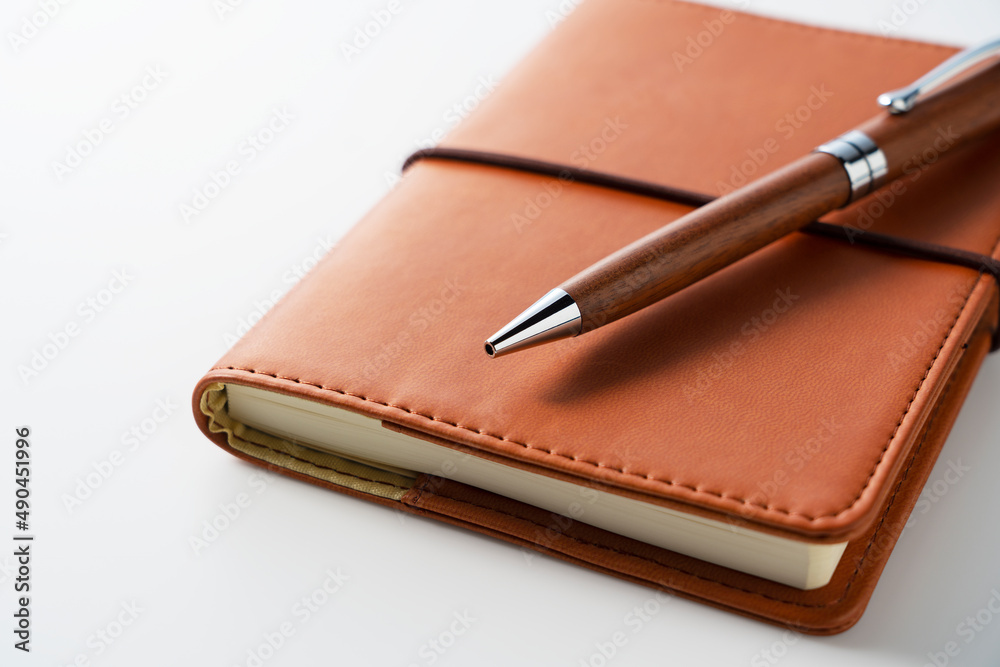 A leather notebook and pen set against a white background.