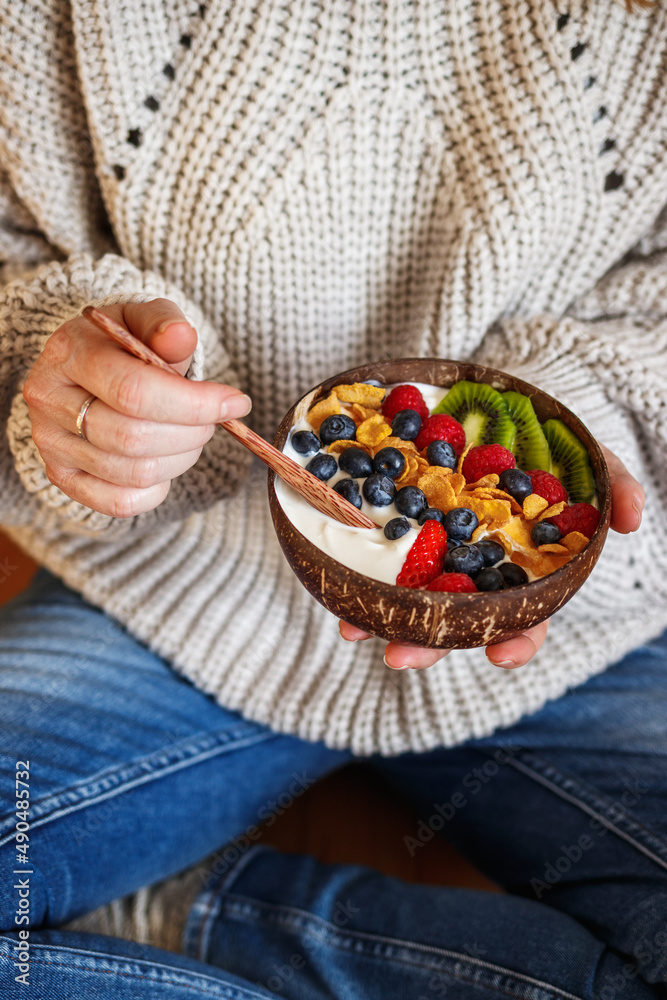 Healthy breakfast at home. Woman sitting on floor and eating yoghurt with fruit and corn flakes. Veg