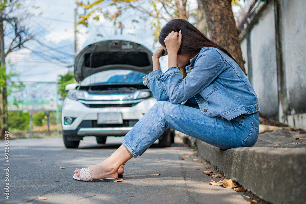 Asian woman sitting beside car after a car breakdown on street. Concept of vehicle engine problem or