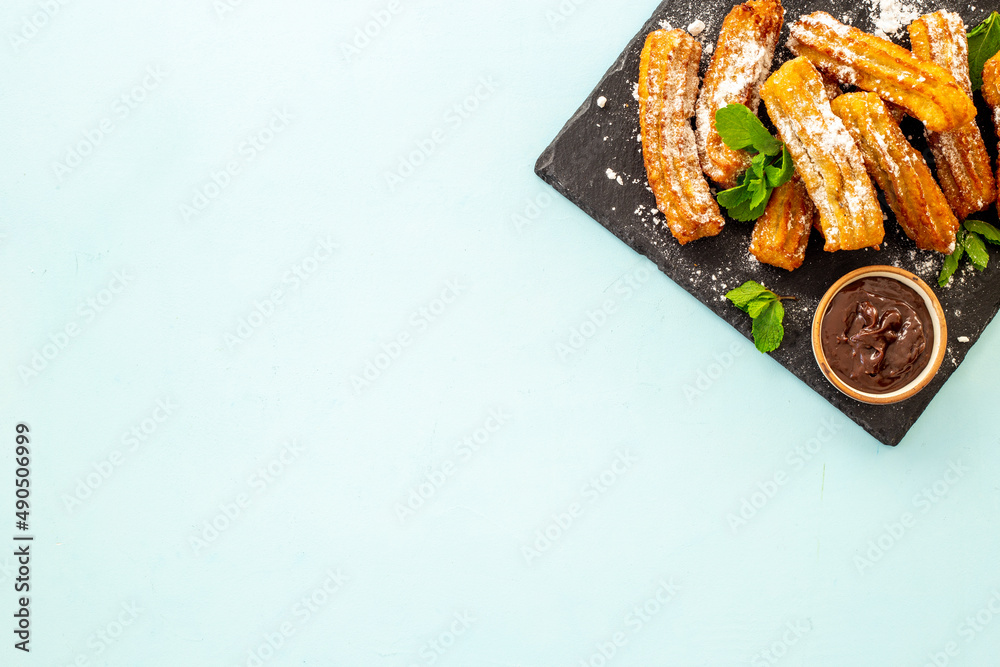 Plate with fried churros and chocolate sauce, top view