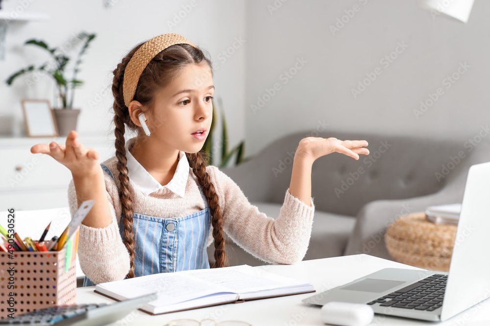 Little girl in earphones studying Literature with online tutor at home