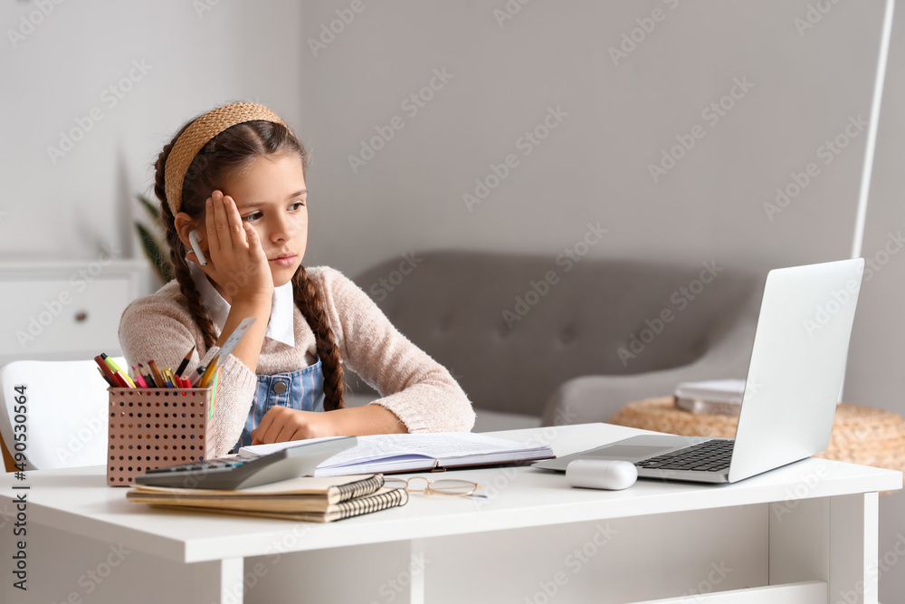 Little girl in earphones studying Literature with online tutor at home