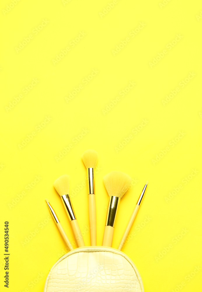 Composition with set of makeup brushes in bag on yellow background