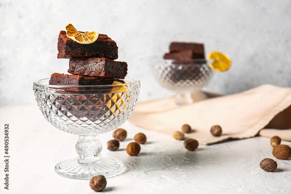 Glass bowl with pieces of delicious chocolate brownie on light background