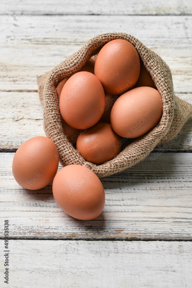 Sack with chicken eggs on white wooden background