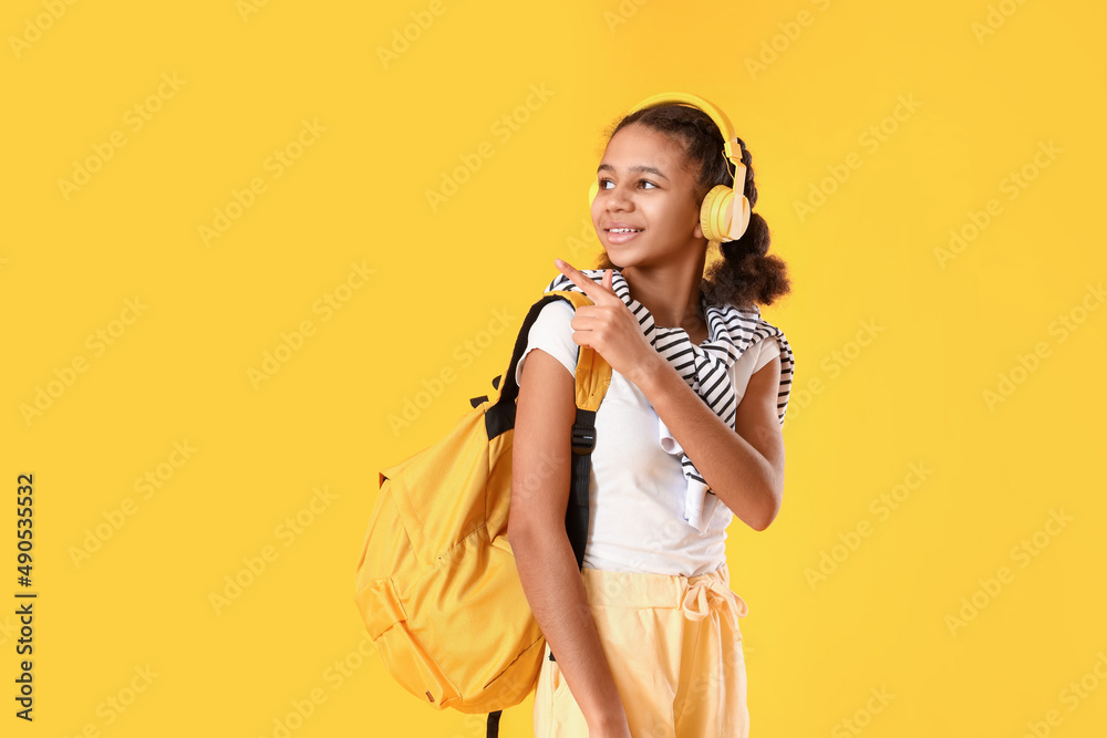 African-American female student listening to music and pointing at something on yellow background