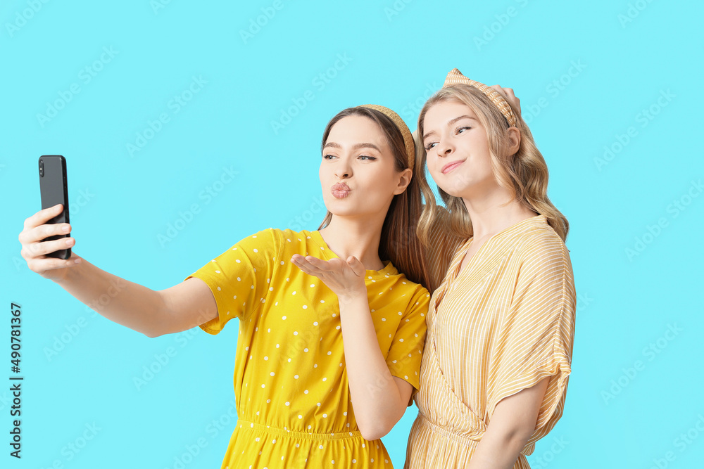 Portrait of happy young sisters taking selfie on color background