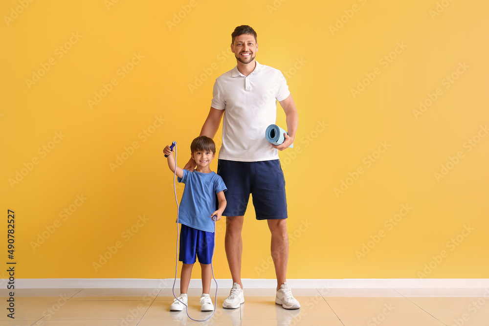 Little boy and his father with sports equipment near yellow wall