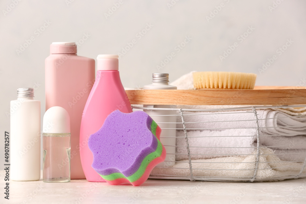 Bottles of cosmetic products, massage brush, bath sponge and clean towels on light background, close