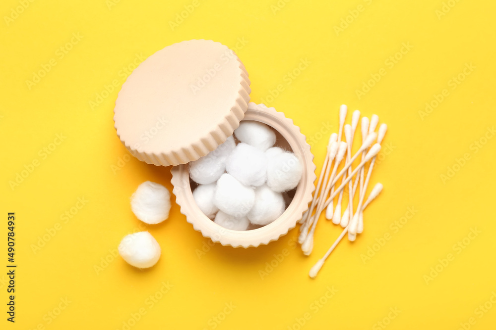 Bowl with cotton balls and swabs on yellow background