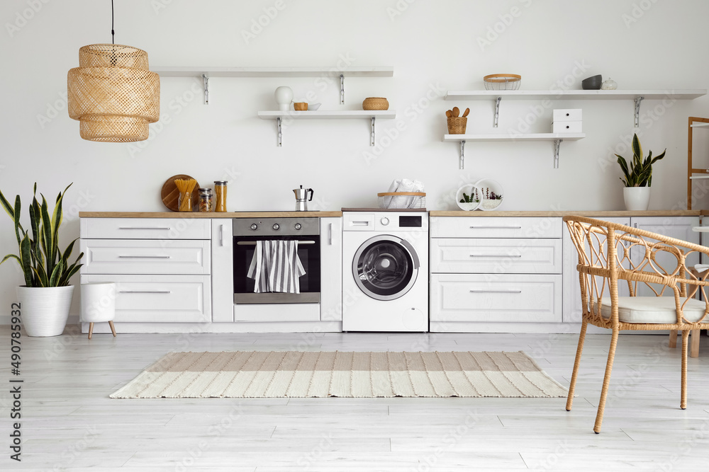 Interior of light kitchen with washing machine, oven and white counters