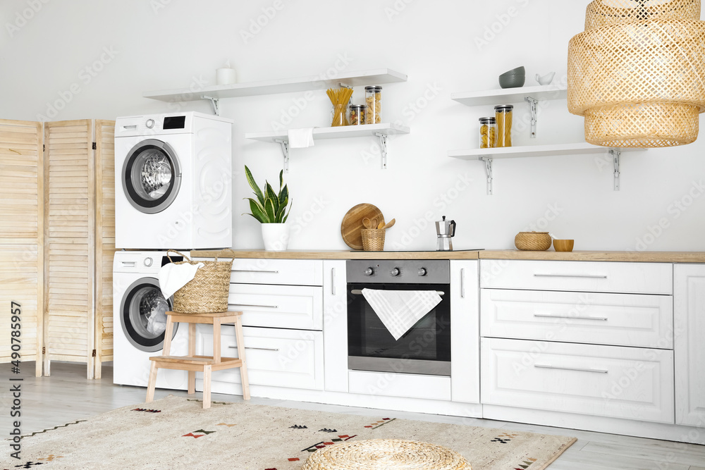 Interior of light kitchen with washing machines, white counters and shelves