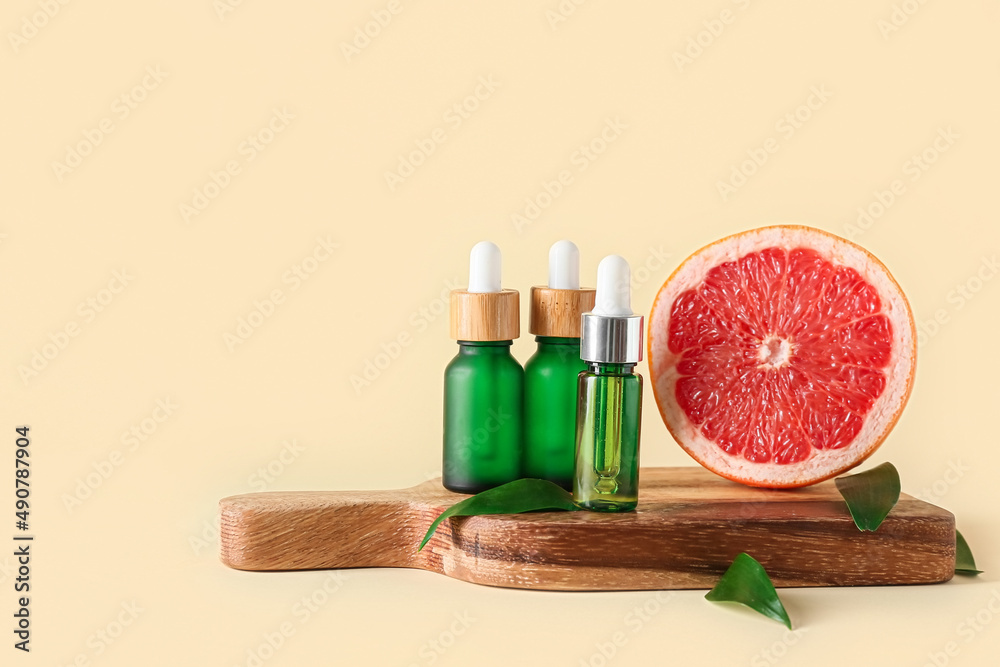 Wooden board with bottles of essential oil and grapefruit on color background