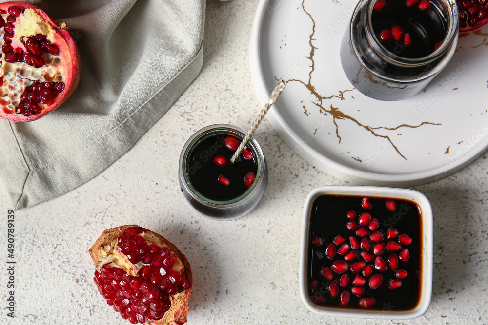 Jars and bowl of pomegranate molasses on light background