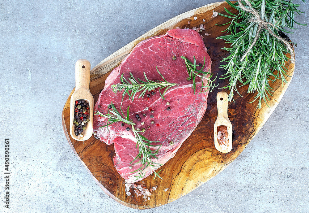 Raw beef steak on wooden board with pepper and salt in wooden spoon and rosemary