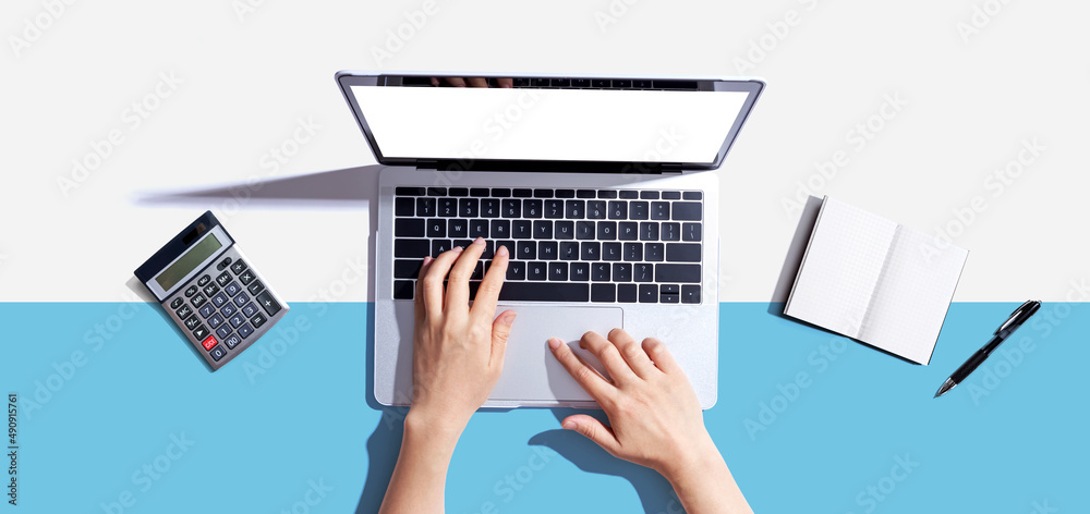 Person using a laptop computer with a notebook and a calculator - flat lay