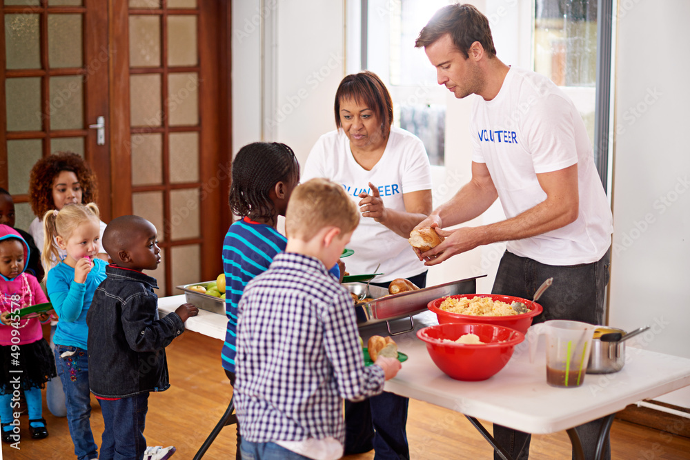 Theres plenty for everyone. Shot of volunteers serving food to a group of little children.