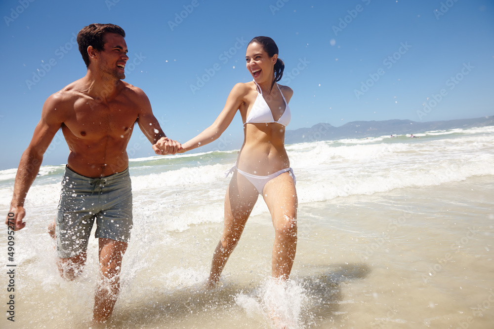 Lets paint this beach red. Shot of a playful couple running through the water at the beach.