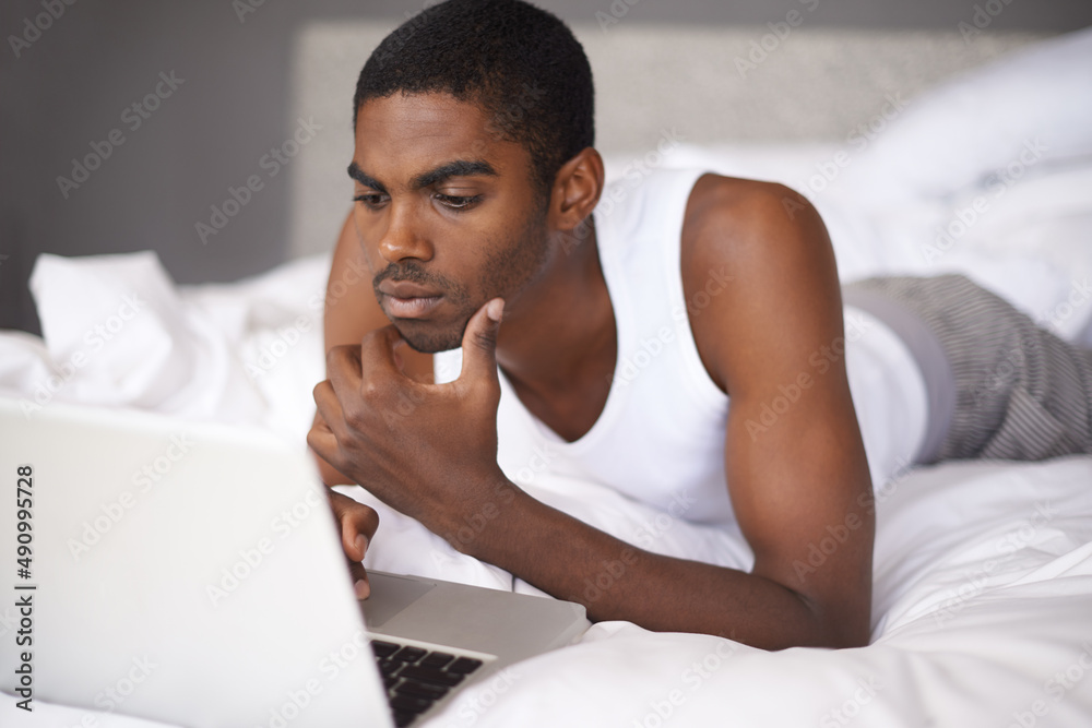 Connected in the morning. Shot of a young man in bed using a laptop.