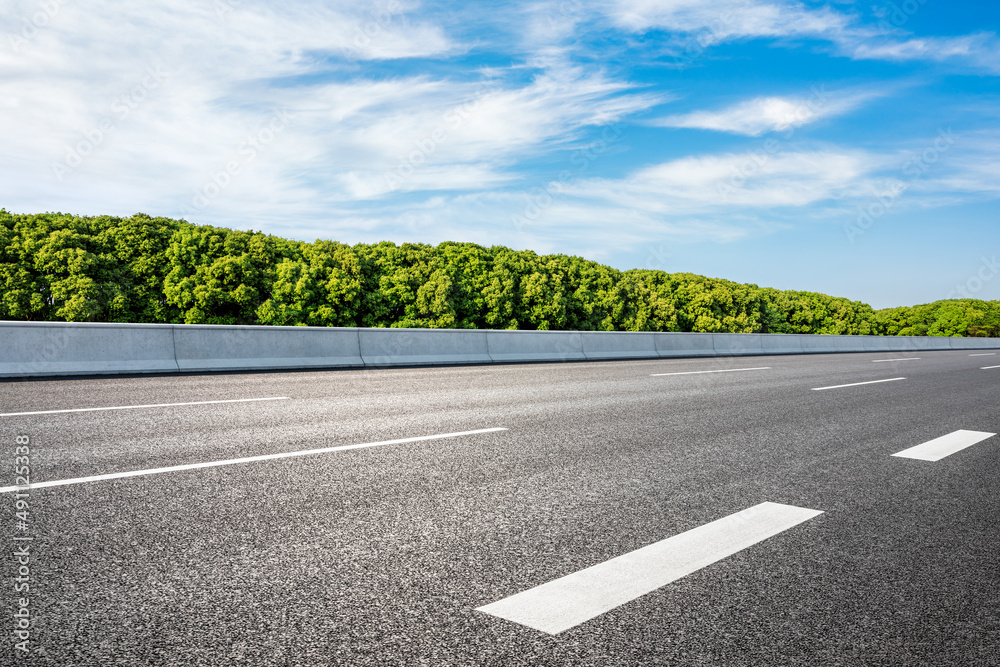 空旷的柏油路和蓝天下的绿色森林。道路和森林背景。